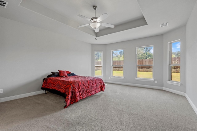 carpeted bedroom featuring a tray ceiling, baseboards, visible vents, and ceiling fan