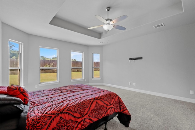 carpeted bedroom featuring a tray ceiling, baseboards, multiple windows, and visible vents