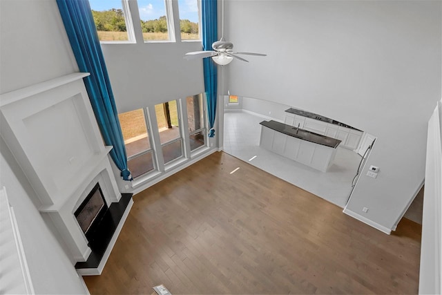 unfurnished living room with ceiling fan, baseboards, a fireplace with raised hearth, and wood finished floors