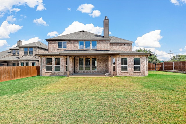 back of property with a lawn, a patio, a fenced backyard, brick siding, and a chimney