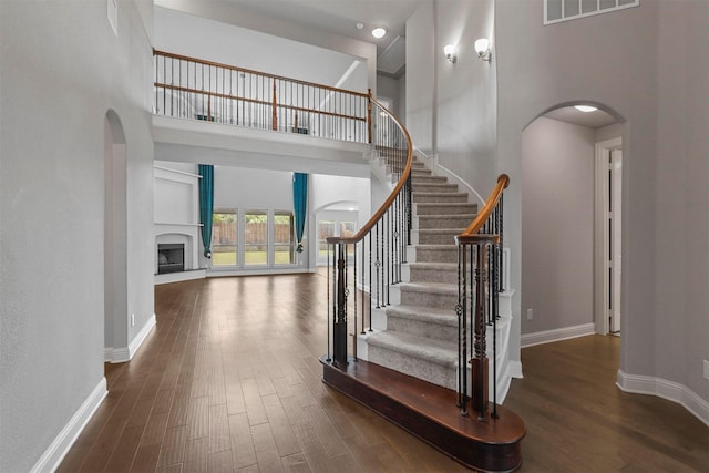 staircase featuring visible vents, arched walkways, a fireplace with raised hearth, and wood finished floors