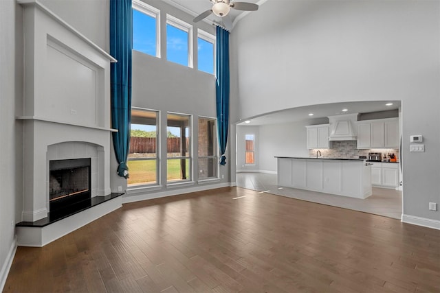 unfurnished living room featuring a fireplace with raised hearth, a ceiling fan, arched walkways, light wood finished floors, and baseboards