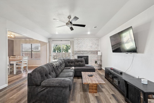 living room with visible vents, a brick fireplace, baseboards, wood finished floors, and a ceiling fan