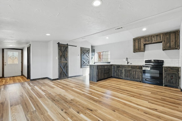 kitchen featuring black electric range oven, a sink, a barn door, a peninsula, and light wood finished floors