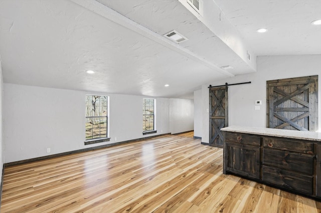 living room with light wood finished floors, visible vents, baseboards, lofted ceiling with beams, and a barn door