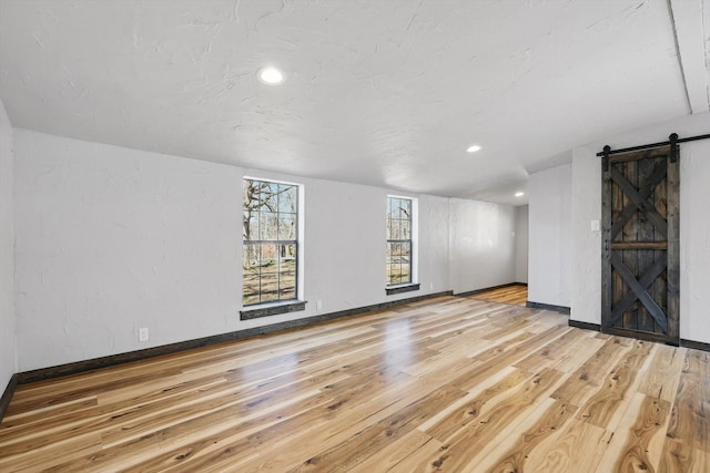 unfurnished living room with recessed lighting, baseboards, a barn door, and wood-type flooring