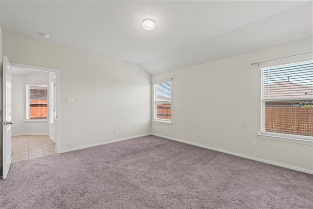 carpeted empty room featuring baseboards, tile patterned flooring, and vaulted ceiling