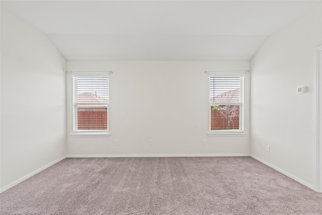 carpeted spare room featuring a healthy amount of sunlight, baseboards, and vaulted ceiling