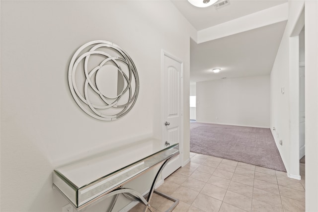 hall featuring light tile patterned flooring, visible vents, light colored carpet, and baseboards