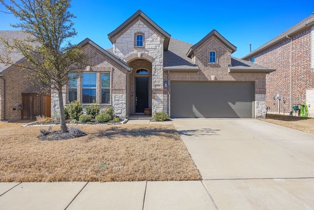 french country home featuring stone siding, roof with shingles, concrete driveway, an attached garage, and brick siding