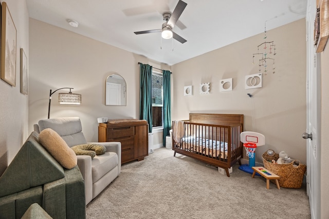 carpeted bedroom with a nursery area and a ceiling fan