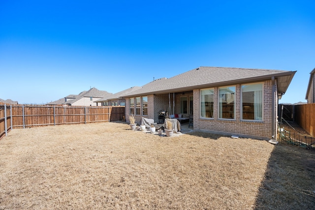 rear view of house featuring a patio, a fenced backyard, brick siding, and a shingled roof