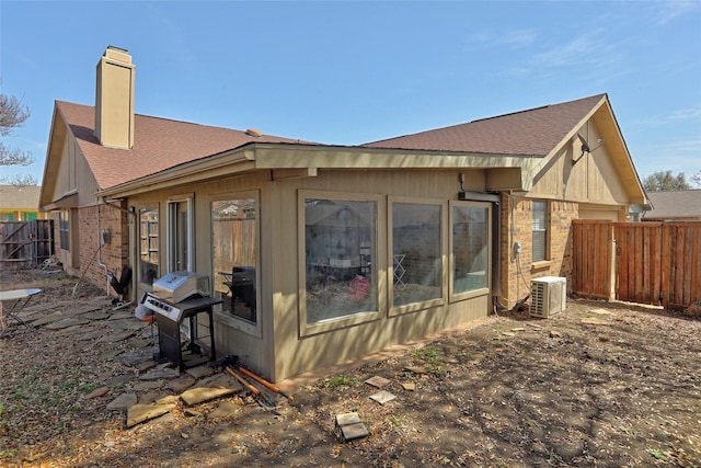 view of side of property with brick siding, a shingled roof, fence, ac unit, and a chimney