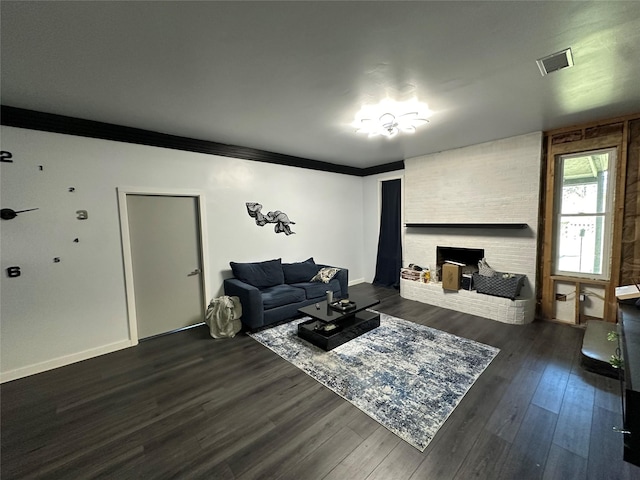 living area with visible vents, dark wood-style floors, crown molding, baseboards, and a brick fireplace