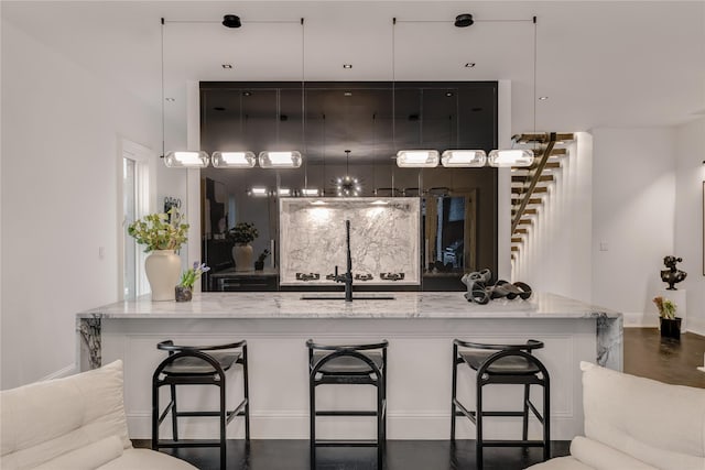 kitchen featuring hanging light fixtures, a sink, a breakfast bar, and light stone countertops