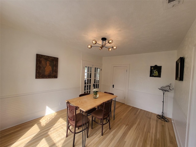 dining area featuring a chandelier, visible vents, light wood-style flooring, and a textured ceiling