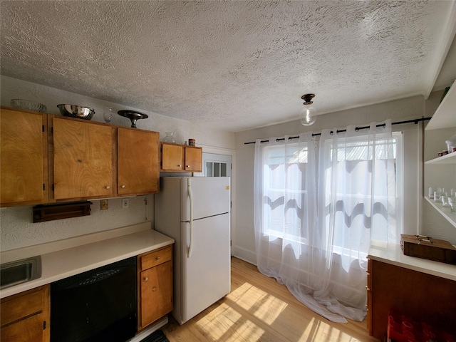 kitchen with black dishwasher, freestanding refrigerator, brown cabinetry, light wood finished floors, and light countertops