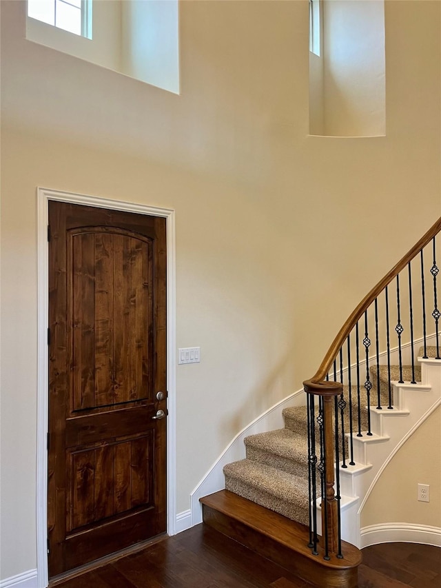 staircase with baseboards, wood finished floors, and a towering ceiling