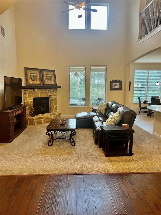 living area featuring visible vents, ceiling fan, a stone fireplace, hardwood / wood-style flooring, and a towering ceiling