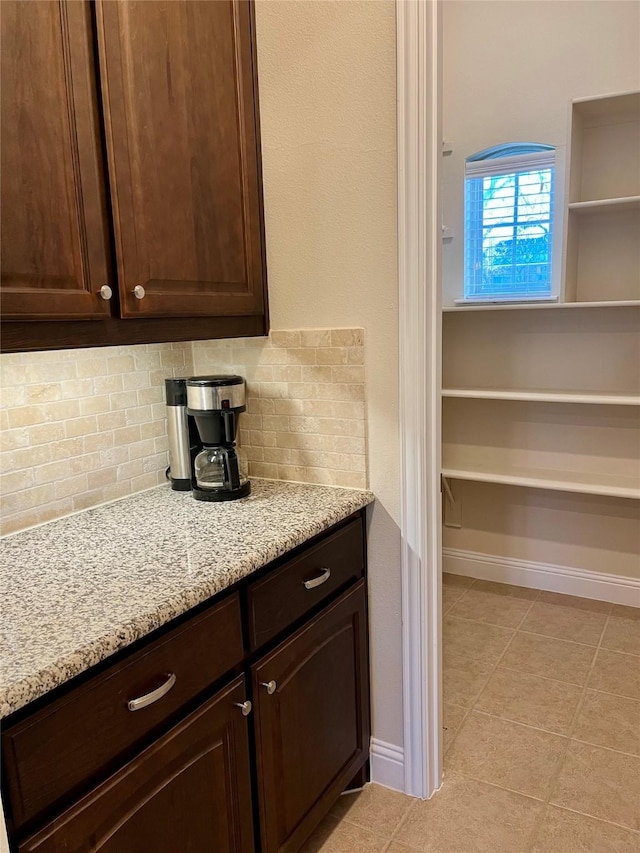 kitchen featuring light stone counters, baseboards, tasteful backsplash, and dark brown cabinets