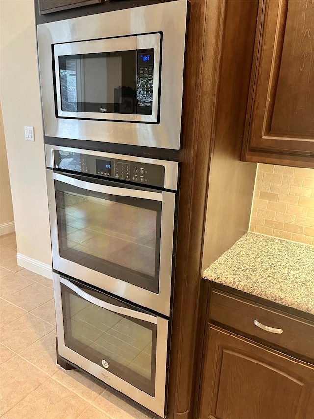 kitchen featuring backsplash, stainless steel appliances, baseboards, light tile patterned floors, and light stone countertops