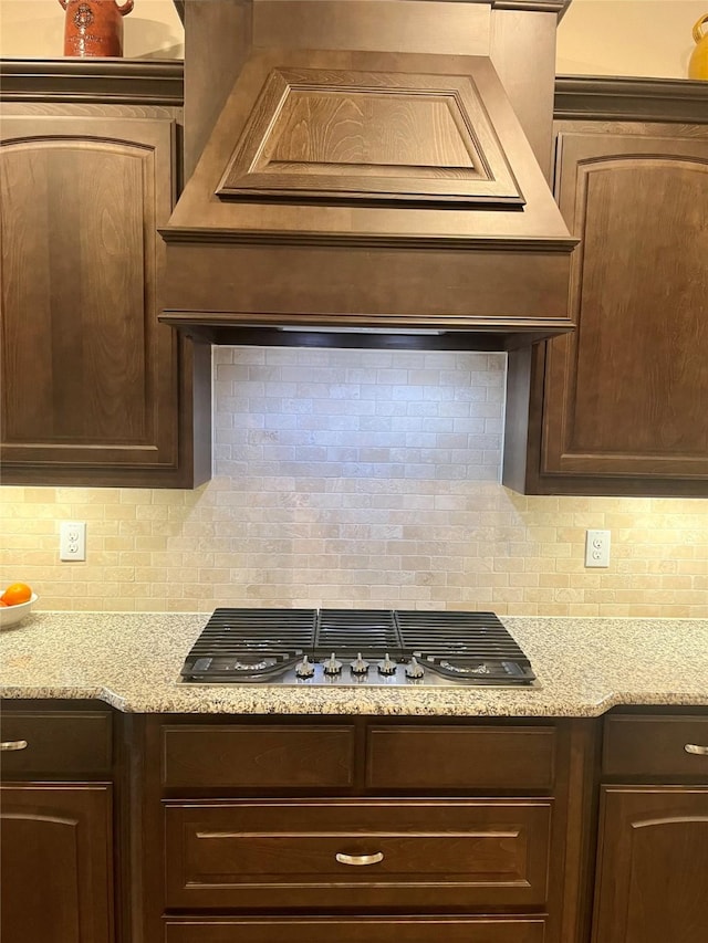 kitchen with decorative backsplash, light stone countertops, dark brown cabinetry, and stainless steel gas stovetop