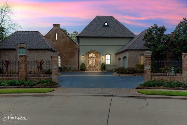 french country inspired facade with fence, brick siding, driveway, and stucco siding