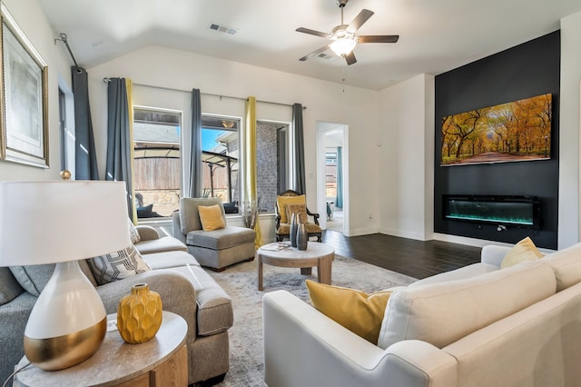 living room with visible vents, lofted ceiling, wood finished floors, a glass covered fireplace, and a ceiling fan