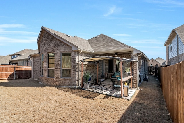 rear view of house featuring brick siding, a fenced backyard, a shingled roof, and a patio