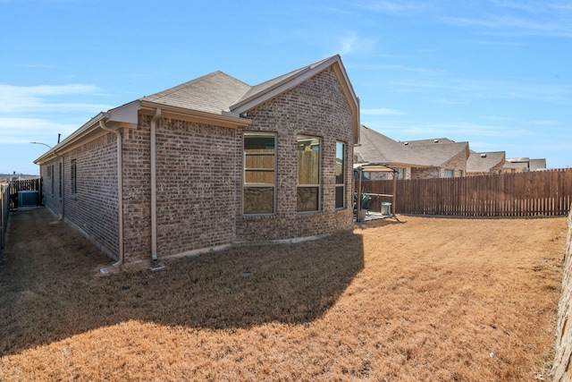 view of side of home with a yard, fence, and brick siding