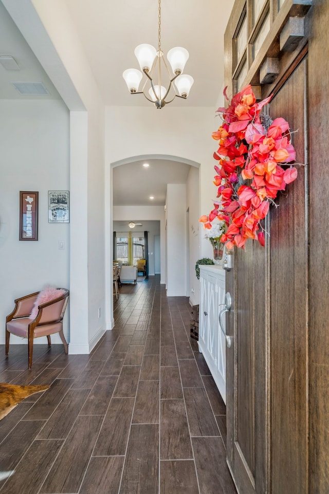 foyer featuring visible vents, baseboards, wood tiled floor, arched walkways, and a notable chandelier