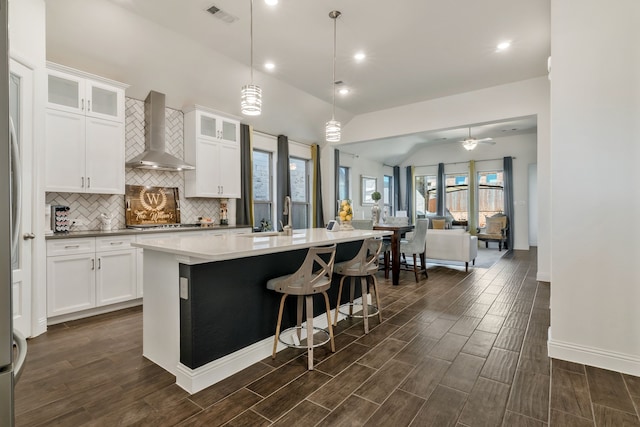 kitchen featuring visible vents, an island with sink, tasteful backsplash, open floor plan, and wall chimney range hood