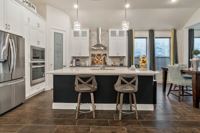 kitchen with a sink, tasteful backsplash, stainless steel appliances, wall chimney exhaust hood, and glass insert cabinets