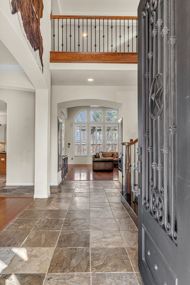 entrance foyer with baseboards, arched walkways, a high ceiling, and stone tile floors