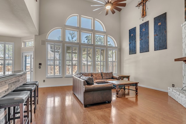 living room featuring a stone fireplace, light wood-style floors, baseboards, and a towering ceiling