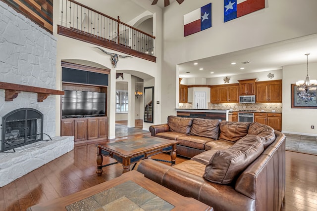 living room featuring a stone fireplace, baseboards, an inviting chandelier, and hardwood / wood-style floors