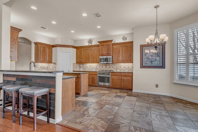 kitchen featuring visible vents, backsplash, a breakfast bar, brown cabinets, and appliances with stainless steel finishes