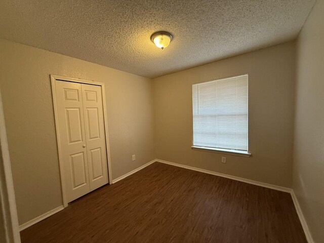 spare room featuring dark wood finished floors, a textured ceiling, and baseboards