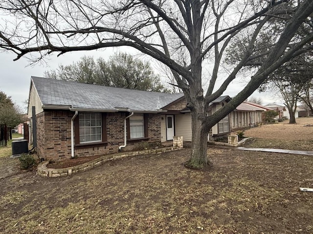 ranch-style home featuring brick siding, central AC, entry steps, and roof with shingles