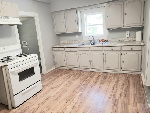 kitchen with light wood-style flooring, under cabinet range hood, a sink, light countertops, and white range with gas stovetop