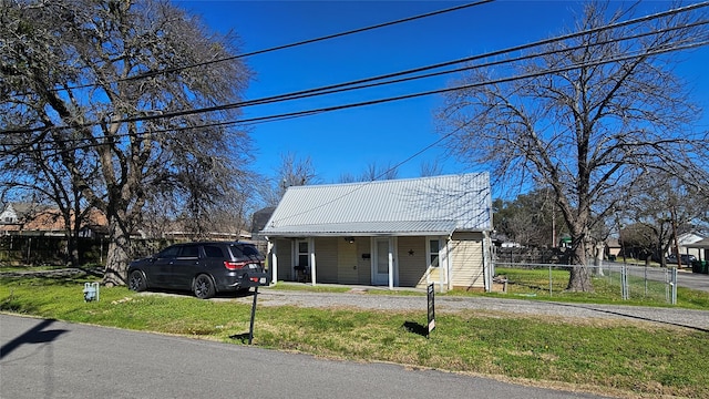 bungalow-style house with dirt driveway, fence, covered porch, a front yard, and metal roof