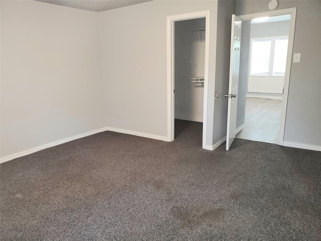 unfurnished bedroom featuring dark colored carpet, a closet, baseboards, and a spacious closet