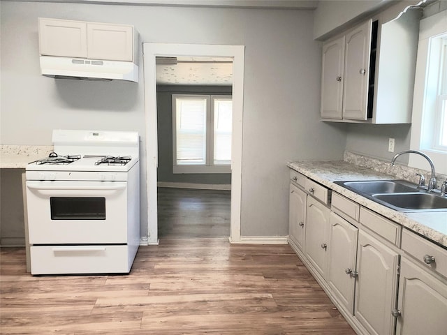 kitchen featuring light wood finished floors, a healthy amount of sunlight, under cabinet range hood, white gas range oven, and a sink