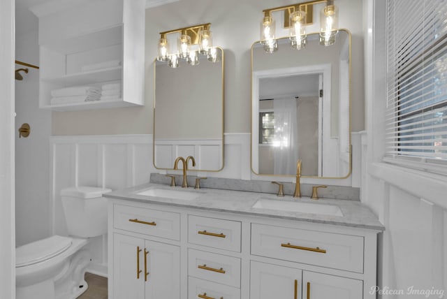 full bath with a sink, toilet, wainscoting, and a decorative wall