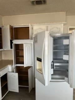 interior space featuring visible vents, open shelves, a textured ceiling, white refrigerator with ice dispenser, and white cabinets