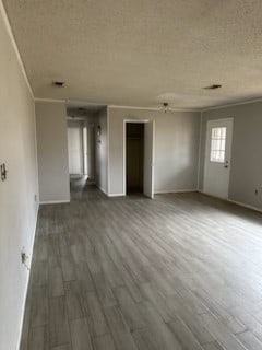 unfurnished living room featuring a textured ceiling, wood finished floors, and ornamental molding