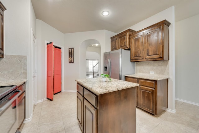 kitchen with tasteful backsplash, a center island, light stone countertops, appliances with stainless steel finishes, and arched walkways