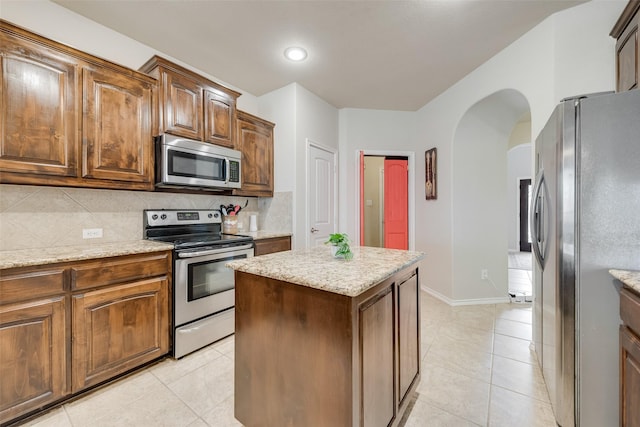 kitchen with arched walkways, decorative backsplash, appliances with stainless steel finishes, and light tile patterned flooring