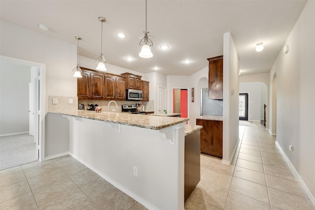 kitchen featuring a breakfast bar area, a peninsula, arched walkways, decorative backsplash, and appliances with stainless steel finishes