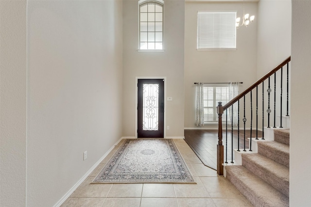 entrance foyer with a notable chandelier, tile patterned flooring, baseboards, a towering ceiling, and stairs